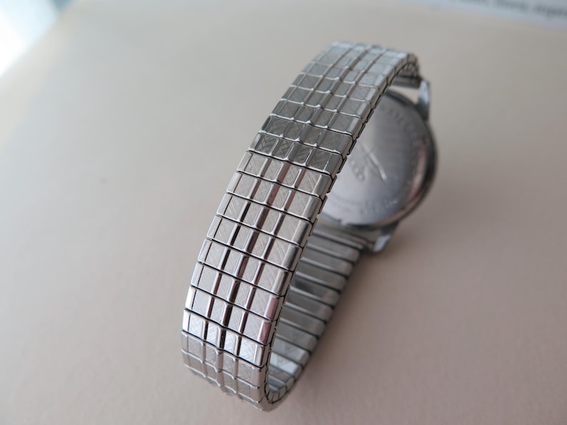 Op de afbeelding: Een zilveren horloge met een metalen band. De wijzerplaat van het horloge is niet zichtbaar. De band is van een metalen gaas.