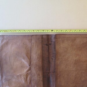 K&ouml;nnte beinhalten: Offenes, braunes Lederjournal mit einem gelben Ma&szlig;band oben. Das Journal ist ge&ouml;ffnet und zeigt die Innenseiten. Das Ma&szlig;band zeigt eine L&auml;nge von etwa 56 cm.