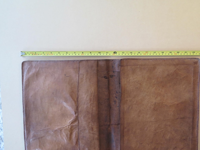 K&ouml;nnte beinhalten: Offenes, braunes Lederjournal mit einem gelben Ma&szlig;band oben. Das Journal ist ge&ouml;ffnet und zeigt die Innenseiten. Das Ma&szlig;band zeigt eine L&auml;nge von etwa 56 cm.