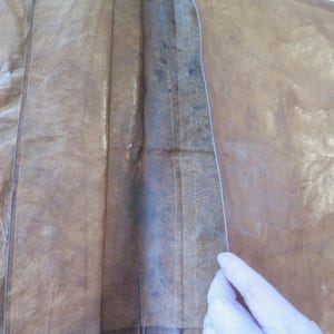 K&ouml;nnte beinhalten: Ein braunes Lederjournal, ge&ouml;ffnet, um das Innere zu zeigen. Das Leder hat ein strukturiertes, abgenutztes Aussehen mit sichtbaren Falten und Farbvariationen. Der Buchr&uuml;cken des Journals ist sichtbar, und die Seiten sind heller.