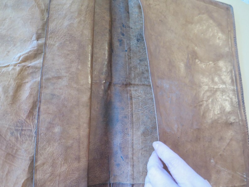 K&ouml;nnte beinhalten: Ein braunes Lederjournal, ge&ouml;ffnet, um das Innere zu zeigen. Das Leder hat ein strukturiertes, abgenutztes Aussehen mit sichtbaren Falten und Farbvariationen. Der Buchr&uuml;cken des Journals ist sichtbar, und die Seiten sind heller.