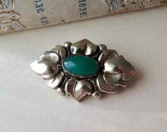 May include: A silver brooch with a green stone set in a floral design.