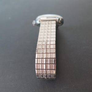 Op de afbeelding: Een zilveren horloge met een metalen band. De band is gemaakt van kleine, vierkante schakels.
