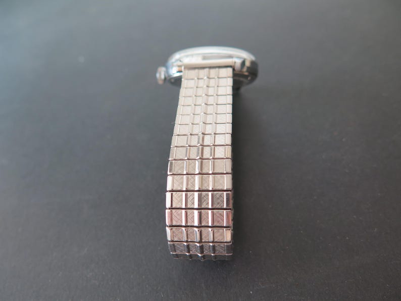 Op de afbeelding: Een zilveren horloge met een metalen band. De band is gemaakt van kleine, vierkante schakels.