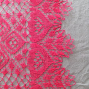 May include: A pink crocheted lace shawl with a delicate floral pattern. The shawl is made with a fine yarn and has a soft, flowing texture.