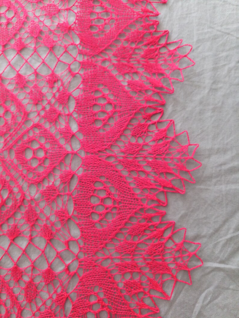 May include: A pink crocheted lace shawl with a delicate floral pattern. The shawl is made with a fine yarn and has a soft, flowing texture.