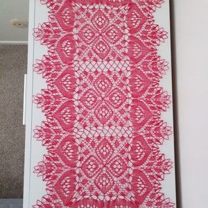 May include: A pink crocheted table runner with a delicate floral pattern. The runner is made with a fine thread and has a lacy appearance.