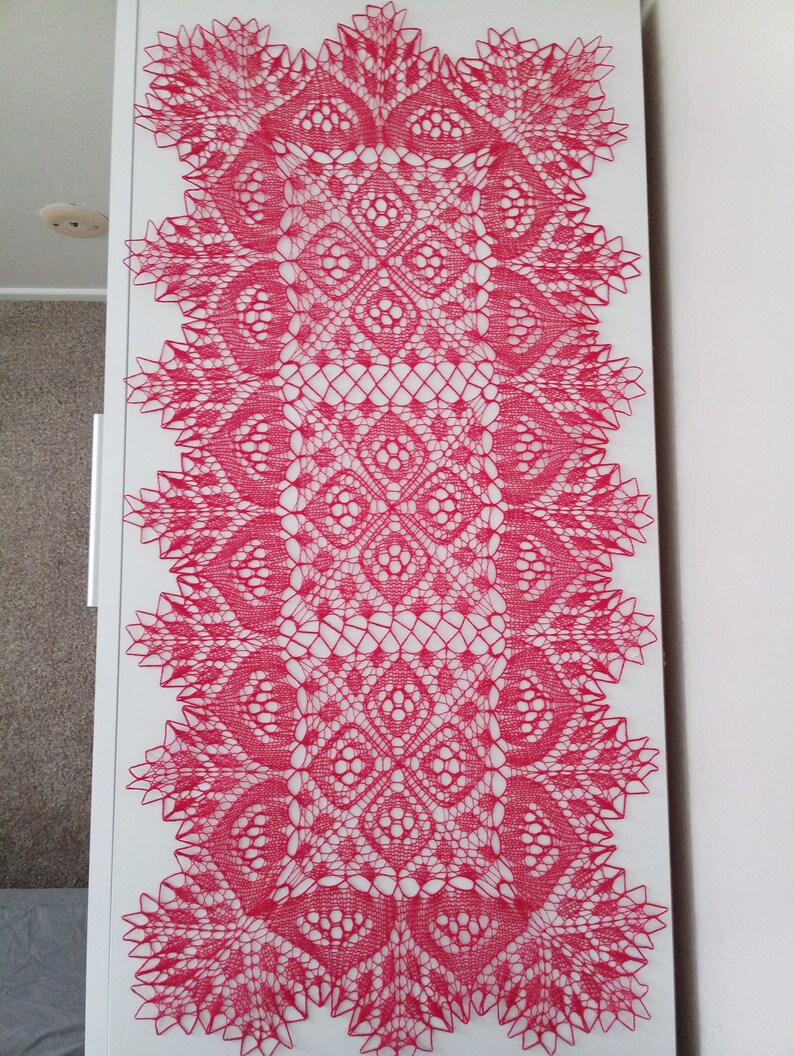 May include: A pink crocheted table runner with a delicate floral pattern. The runner is made with a fine thread and has a lacy appearance.