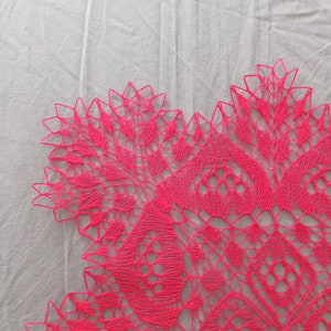 May include: A pink crocheted doily with a delicate floral pattern. The doily is made with fine yarn and has a lacy, intricate design.