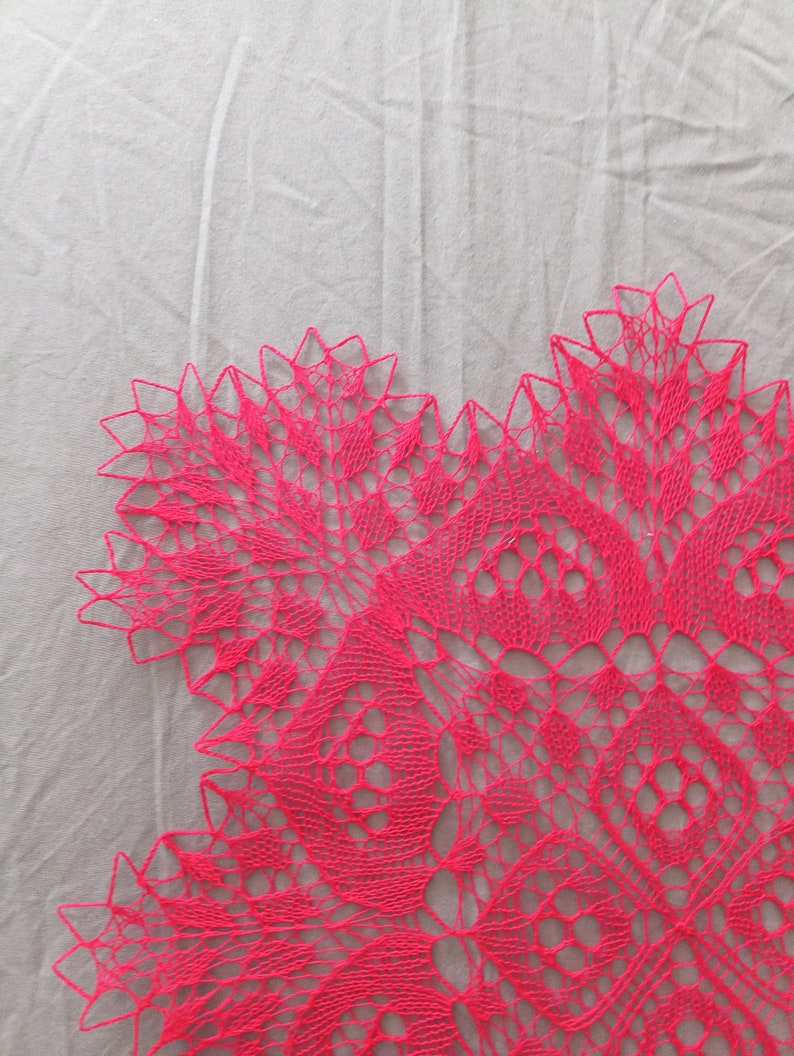 May include: A pink crocheted doily with a delicate floral pattern. The doily is made with fine yarn and has a lacy, intricate design.