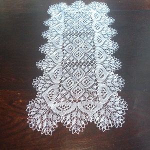 May include: White crocheted table runner with a delicate floral pattern. The runner is made of fine thread and has a lacy design.