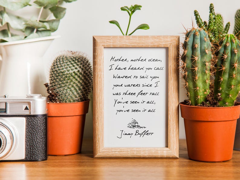 May include: A framed print with a handwritten lyric from the song "Mother, Mother Ocean" by Jimmy Buffett. The lyric reads: "Mother, mother ocean, I have heard you call Wanted to sail upon your waters since I was three feet tall You've seen it all, you've seen it all".