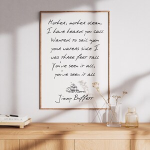 May include: A framed print with a white background and black text. The text reads "Mother, mother ocean, I have heard you call Wanted to sail upon your waters since I was three feet tall You've seen it all, you've seen it all" and is signed "Jimmy Buffett".