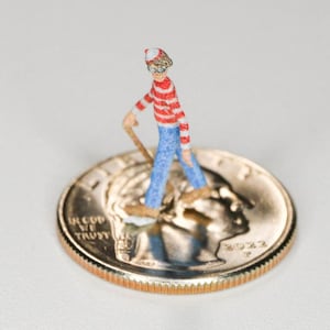 May include: A miniature figurine of a person wearing a red and white striped shirt, blue jeans, and a red and white hat, standing on a US quarter with the year 2022.