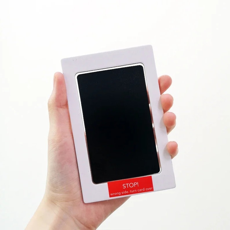 May include: A white and silver baby footprint kit. The kit has a rectangular frame with a black ink pad and a red sticker that reads "STOP! wrong side, turn card over."