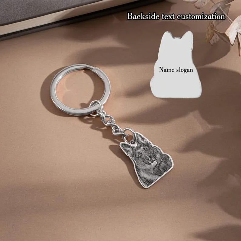 May include: A silver keychain with a dog-shaped pendant. The pendant features a detailed image of a dog's face. The keychain also includes a blank dog-shaped tag with the text "Name slogan" and "Backside text customization".