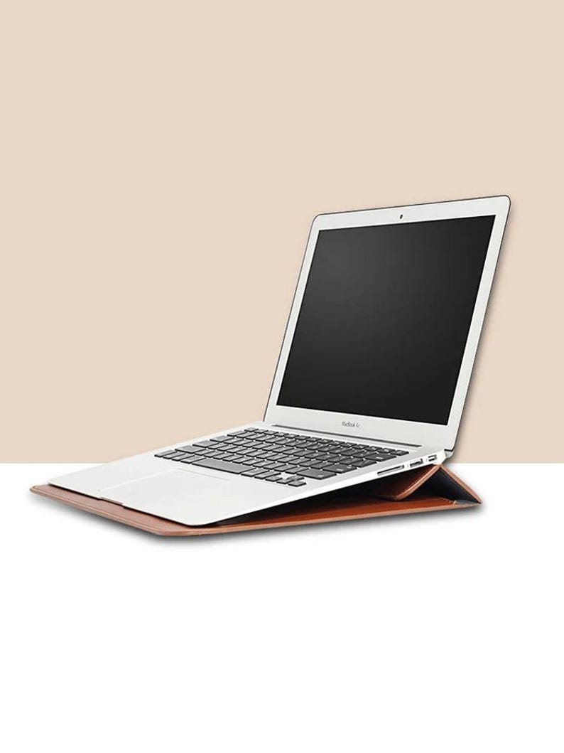 May include: A brown leather laptop case with a silver laptop inside. The laptop is open and the screen is black.