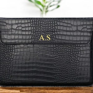 May include: Black leather laptop sleeve with a crocodile embossed pattern and gold initials "A.S."