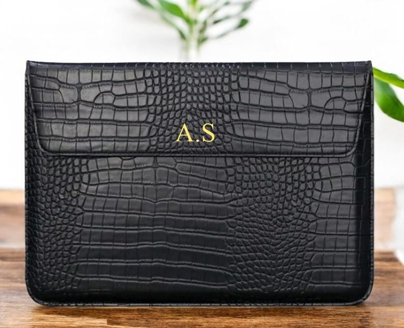 May include: Black leather laptop sleeve with a crocodile embossed pattern and gold initials "A.S."