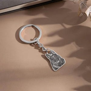 May include: Silver-colored keychain featuring a detailed pendant of a German Shepherd dog. The pendant is attached to a chain and a large key ring. The dog's image is in grayscale, with visible fur and facial features.