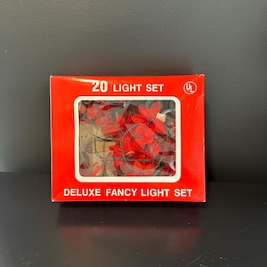 May include: A red box labeled "20 LIGHT SET" with a clear window displaying red flower-shaped lights. The box also reads "DELUXE FANCY LIGHT SET". The lights are on a green wire.