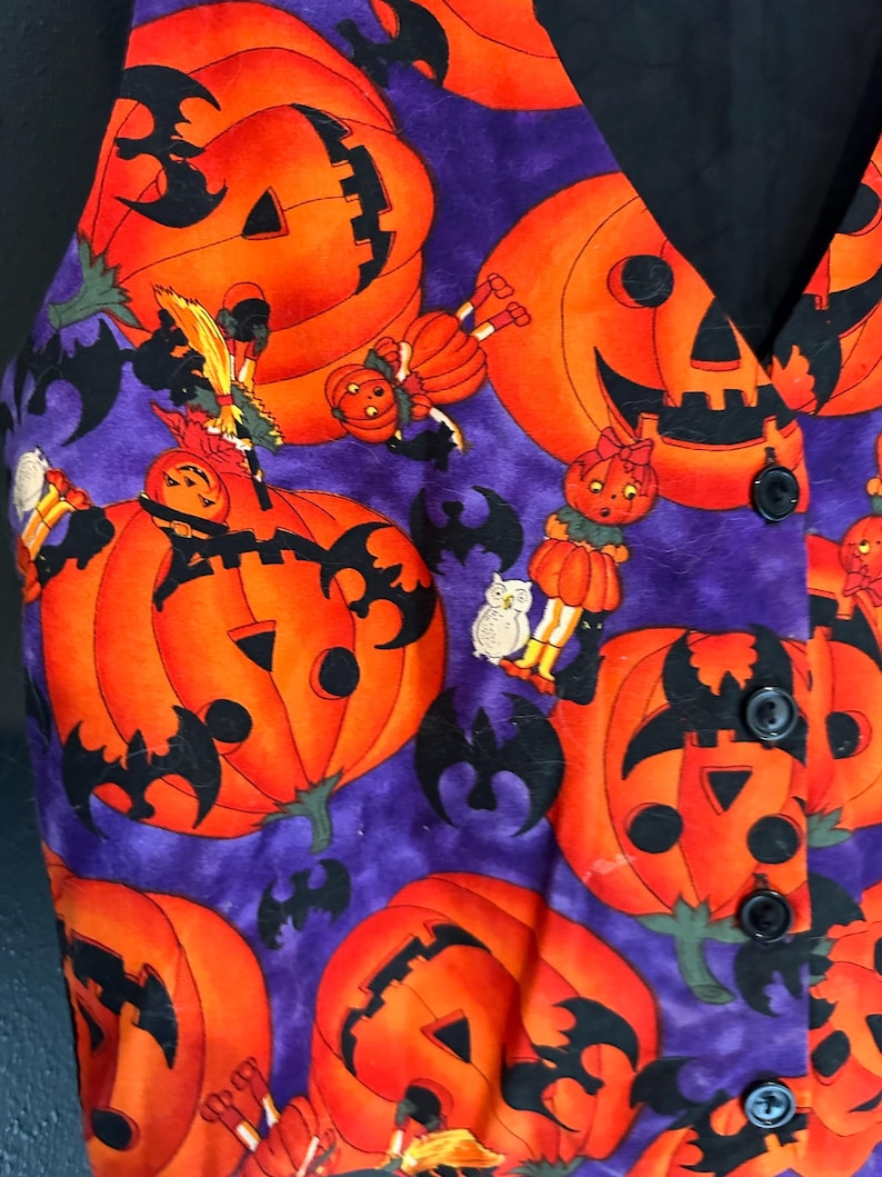 May include: A Halloween-themed vest with a purple background and orange jack-o'-lanterns. Black bats and cartoon figures are scattered across the fabric. The vest has a black collar and buttons.