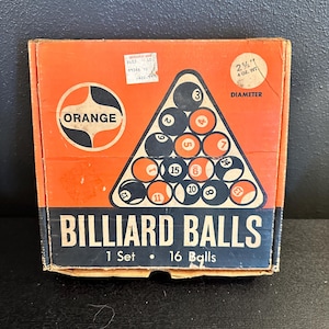 May include: A square cardboard box for a set of 16 billiard balls. The orange and black packaging features a triangular graphic of numbered balls, the text ORANGE, and BILLIARD BALLS 1 Set 16 Balls. A circular label indicates 2 1/4 inch diameter.