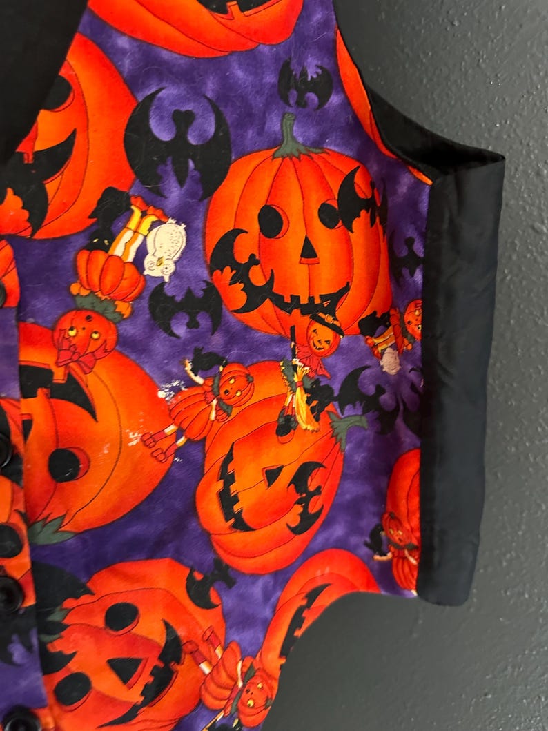 May include: A Halloween-themed vest with a purple background and orange jack-o'-lanterns. Black bats and small figures are scattered across the fabric. The vest has a black trim and buttons.