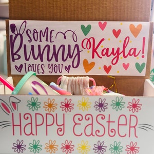 May include: A white cardboard box with a bunny rabbit design and the text "Some Bunny Kayla! Loves You" and "Happy Easter". The box is filled with colorful Easter-themed items.