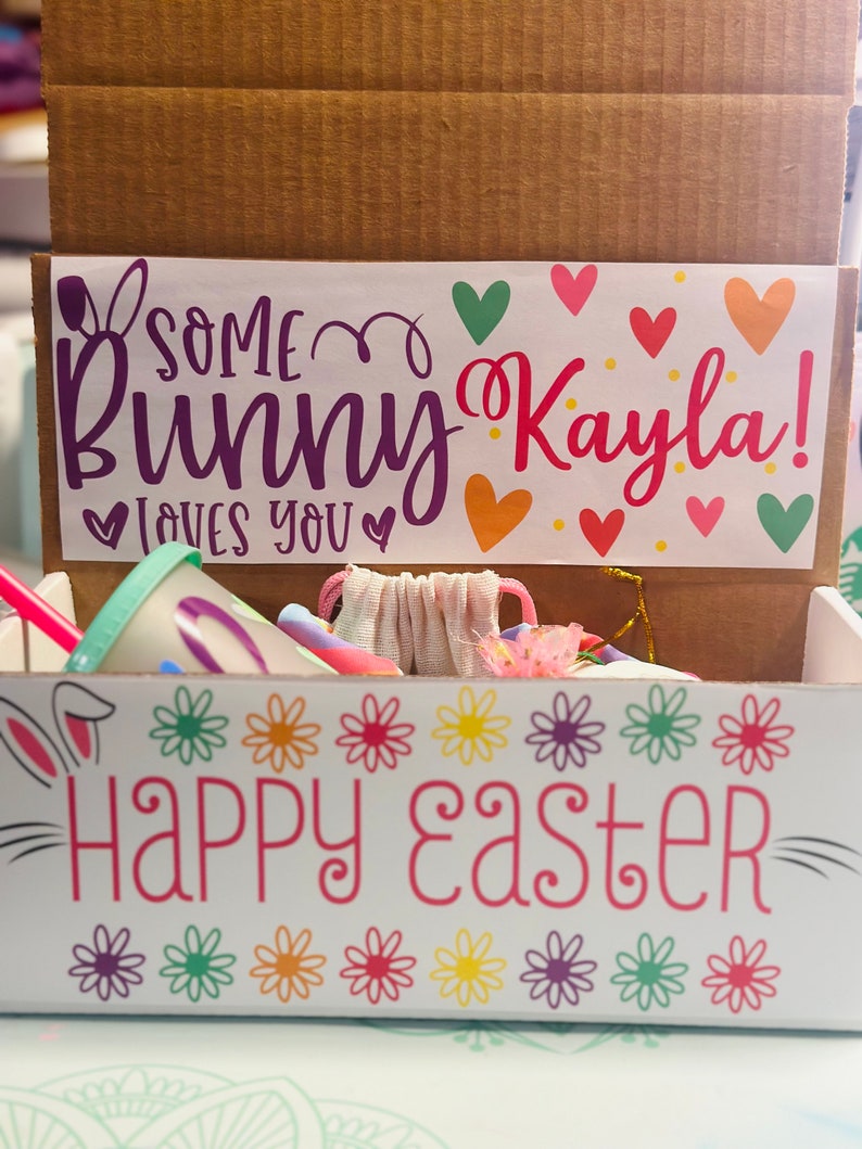 May include: A white cardboard box with a bunny rabbit design and the text "Some Bunny Kayla! Loves You" and "Happy Easter". The box is filled with colorful Easter-themed items.