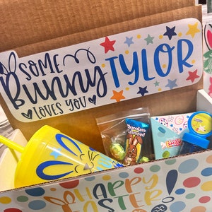 May include: A yellow and blue Easter-themed gift box with a yellow tumbler with a bunny face, a chocolate bunny, and a small bag of candy. The box has a sticker that says "Some bunny loves you" and "Happy Easter!"