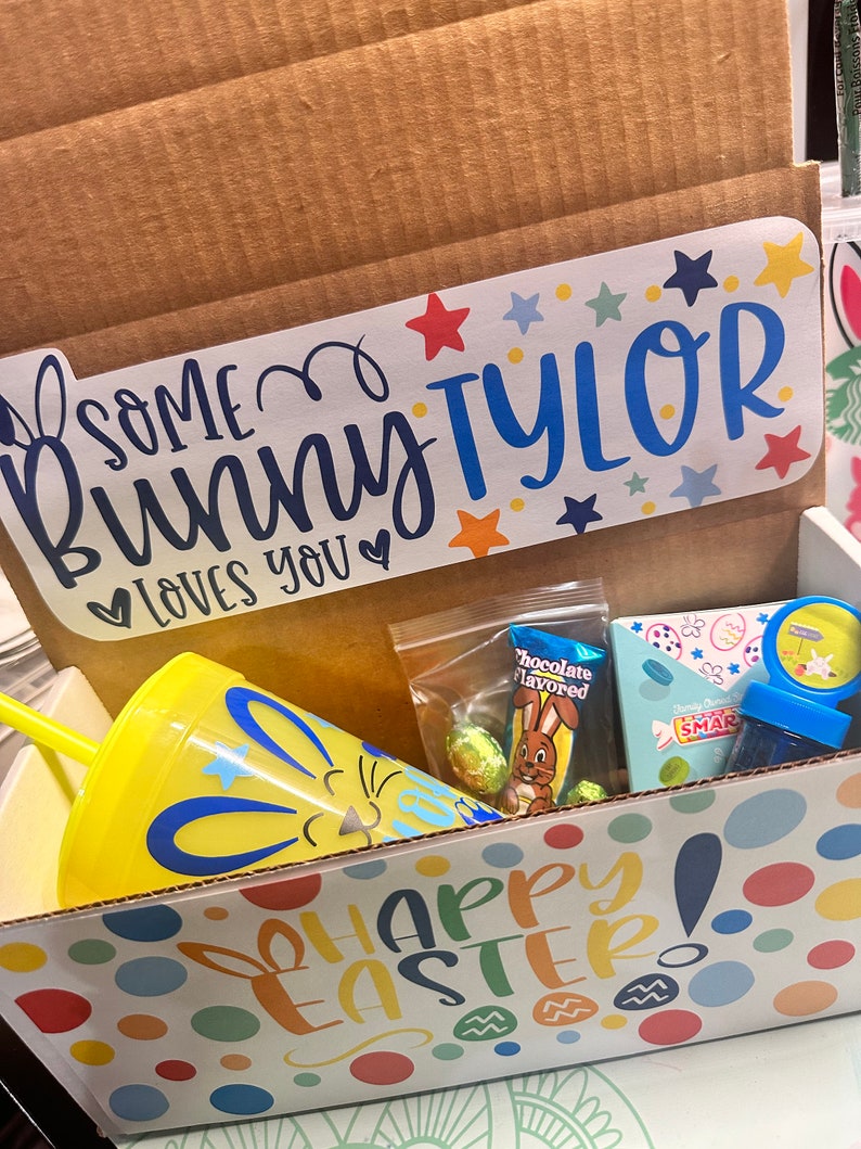 May include: A yellow and blue Easter-themed gift box with a yellow tumbler with a bunny face, a chocolate bunny, and a small bag of candy. The box has a sticker that says "Some bunny loves you" and "Happy Easter!"