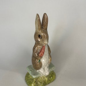 May include: A brown and white ceramic figurine of a rabbit sitting on a green base. The rabbit is holding a carrot in its paws.