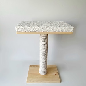May include: A white cat scratching post with a rectangular platform covered in white carpet. The post is made of natural wood and wrapped in white rope.