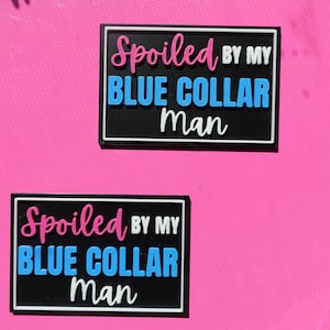 May include: Two black rectangular patches with white borders. The text "Spoiled" is in pink, "BY MY" is in white, "BLUE COLLAR" is in blue, and "Man" is in white. The patches are on a bright pink background.