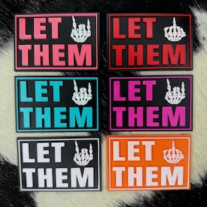 May include: Six rectangular patches with the words "LET THEM" in bold letters. Each patch has a different color scheme: pink, red, teal, magenta, black, and orange. A white skeleton hand with the middle finger raised is on each patch.
