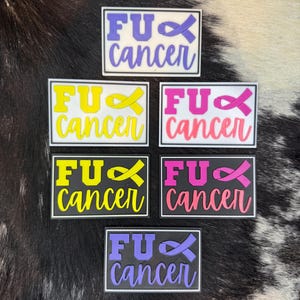 May include: Rectangular patches with the text "FU Cancer" in various colors, including purple, yellow, and pink. Each patch features a ribbon symbol. The patches are displayed on a black and white patterned surface.