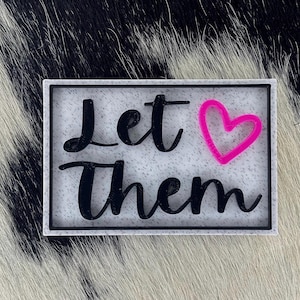 Peut inclure: Panneau rectangulaire avec les mots "Let Them" en écriture noire et un cœur rose. Le panneau a un fond blanc moucheté et une bordure noire. Le fond est un motif de peau de vache noir et blanc.