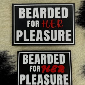 Könnte beinhalten: Zwei schwarze rechteckige Aufnäher mit weißem und rotem Text. Der obere Aufnäher lautet "BEARDED FOR HER PLEASURE" in weißen Blockbuchstaben, mit "HER" in roter Schrift. Der untere Aufnäher hat denselben Text.