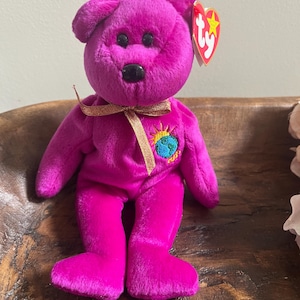 May include: Purple Ty Beanie Baby with a gold ribbon and a patch that says "Ty" and has a picture of the Earth and the sun.