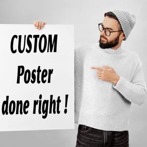 May include: A rectangular white poster featuring the black text CUSTOM Poster done right! in a bold sans-serif font. The poster is held by a person wearing a light grey knit jumper, a matching grey beanie, and dark-rimmed glasses.