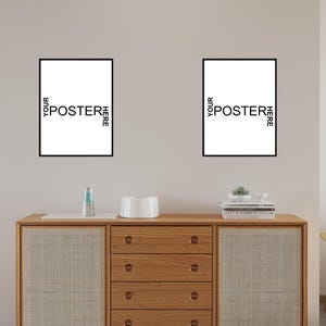 May include: Two rectangular wall posters with thin black frames, each featuring the white text YOUR POSTER HERE arranged in a cross pattern. The posters are displayed side-by-side on a plain wall above a wooden cabinet with four drawers.