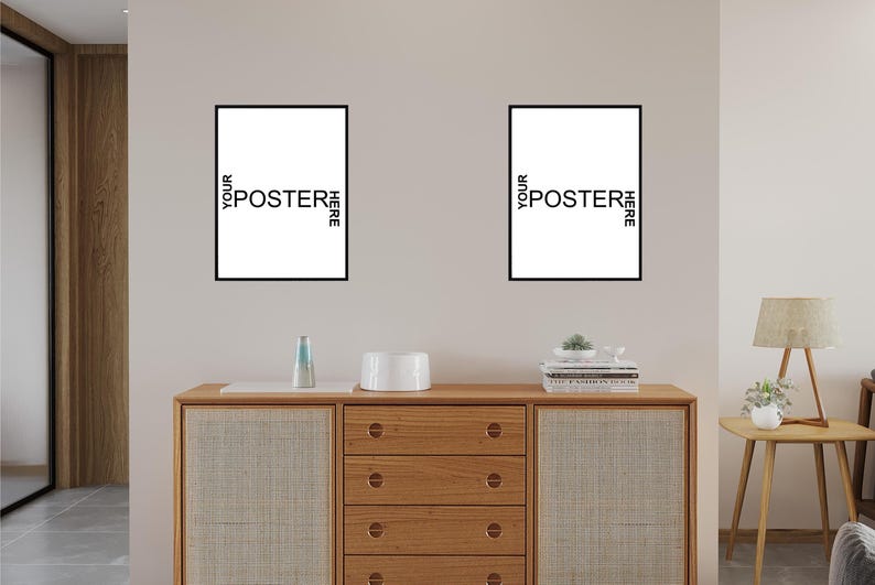 May include: Two rectangular wall posters with thin black frames, each featuring the white text YOUR POSTER HERE arranged in a cross pattern. The posters are displayed side-by-side on a plain wall above a wooden cabinet with four drawers.