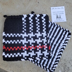 May include: A black, white, and red woven hot pad with a houndstooth pattern and a striped section. The hot pad has a loop for hanging and includes the text "Little Acre Home Shop".