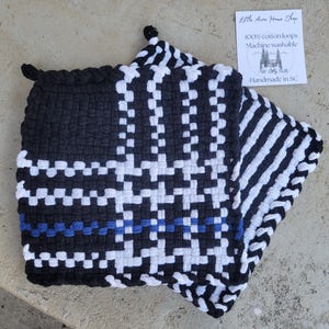 May include: Black and white woven potholder with a blue stripe. The potholder is made of 100% cotton loops and is machine washable. The text "Little Acre Home Shop" is visible in the image.