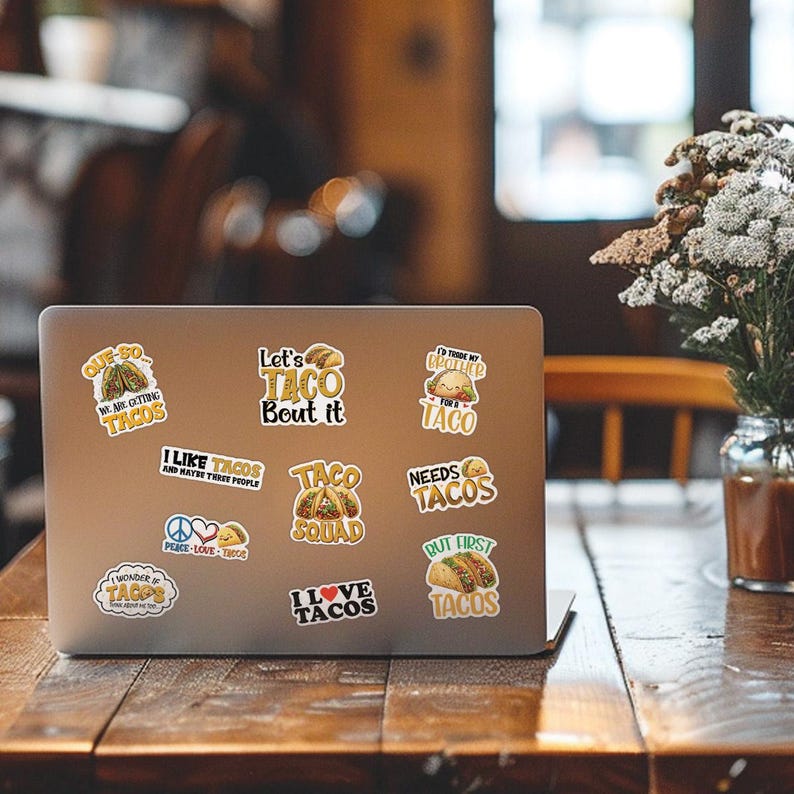 K&ouml;nnte beinhalten: Ein Laptop mit bunten Aufklebern zum Thema Tacos. Die Aufkleber zeigen S&auml;tze wie &bdquo;Let's Taco Bout it&ldquo;, &bdquo;I Love Tacos&ldquo; und &bdquo;Needs Tacos&ldquo;. Die Aufkleber sind in verschiedenen Formen und Gr&ouml;&szlig;en mit Bildern von Tacos.