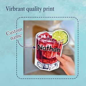 May include: A sticker featuring a glass of red cocktail with ice cubes and a lime slice garnish. The glass has the text Nathan printed on the front. The sticker includes the text Custom name with an arrow pointing to the name and Virbant quality print.