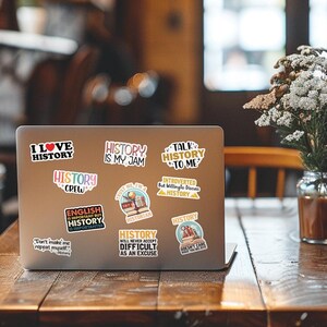 May include: A silver laptop with various colorful stickers featuring history-themed quotes and designs. The stickers include phrases like "I Love History", "History is My Jam", "History Crew", "Talk History to Me", "Introverted But Willing to Discuss History", "English is Important But History is Importanter", "Trust Me I'm a Historian", "History Will Never Accept Difficult as an Excuse", and "History Doesn't Care Who You Believe".