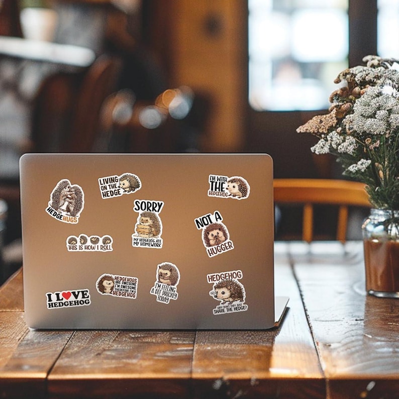 May include: A silver laptop computer with multiple hedgehog-themed stickers. The stickers feature various hedgehog illustrations and text such as "I love hedgehog", "Hedgehugs", "Living on the hedge", "Sorry, my hedgehogs are my homework", "I'm with the hedgehog", "Not a hugger", "Hedgehogs are my favorite animal", "I'm feeling a bit prickly today", and "Who wants to share the hedge?"
