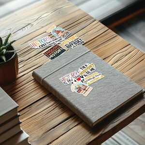 May include: A collection of colorful stickers with text about history. The stickers are on a gray notebook. The text on the stickers includes "History is my jam", "History talk to me", "Introverted but willing to discuss history", "English is important but history is more important", "Don't make me repeat myself", "History will never accept difficult as an excuse".